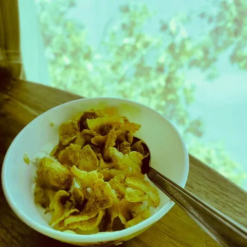A white bowl of vanilla ice cream covered with syrup-coated cornflakes, with a spoon resting in it