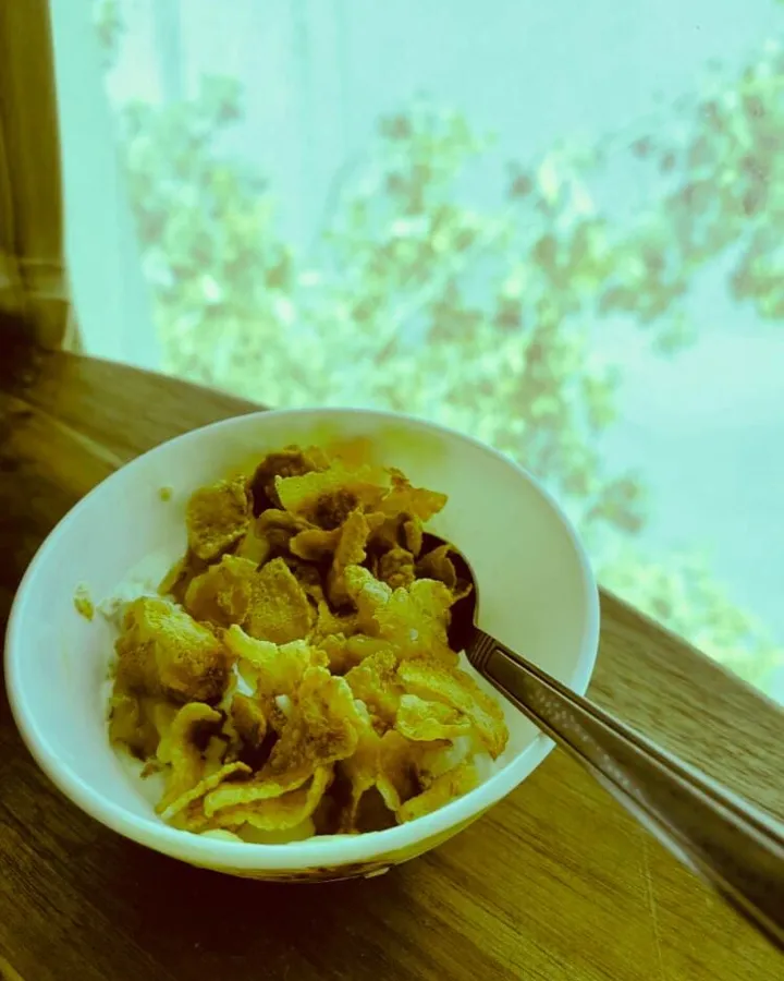 A white bowl of vanilla ice cream covered with syrup-coated cornflakes, with a spoon resting in it