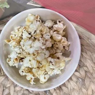 A white bowl of homemade stovetop popcorn on a woven placemat