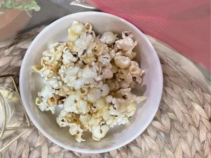 A white bowl of homemade stovetop popcorn on a woven placemat