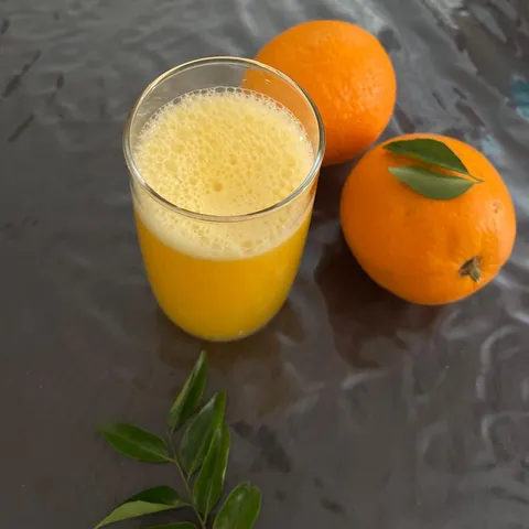 A glass of fresh homemade orange juice next to two whole oranges