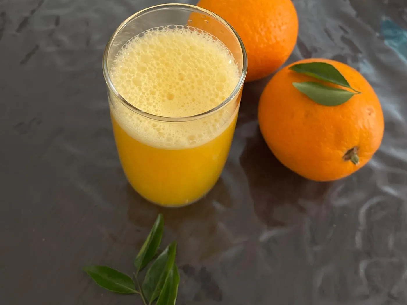 A glass of fresh homemade orange juice next to two whole oranges