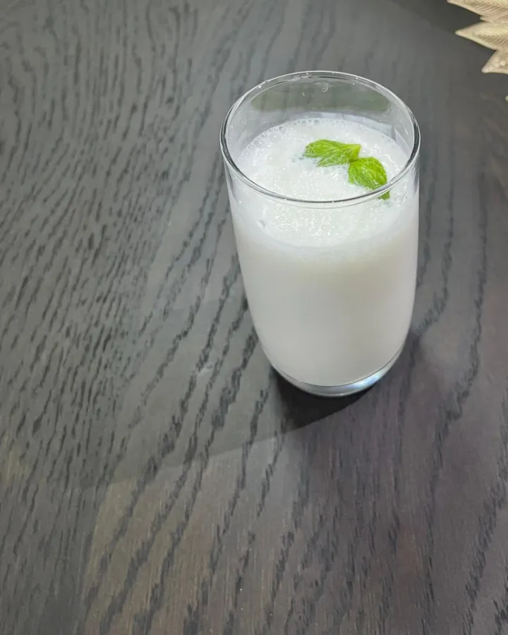 A tall glass of chilled laban yogurt drink garnished with mint leaves, on a dark wooden table