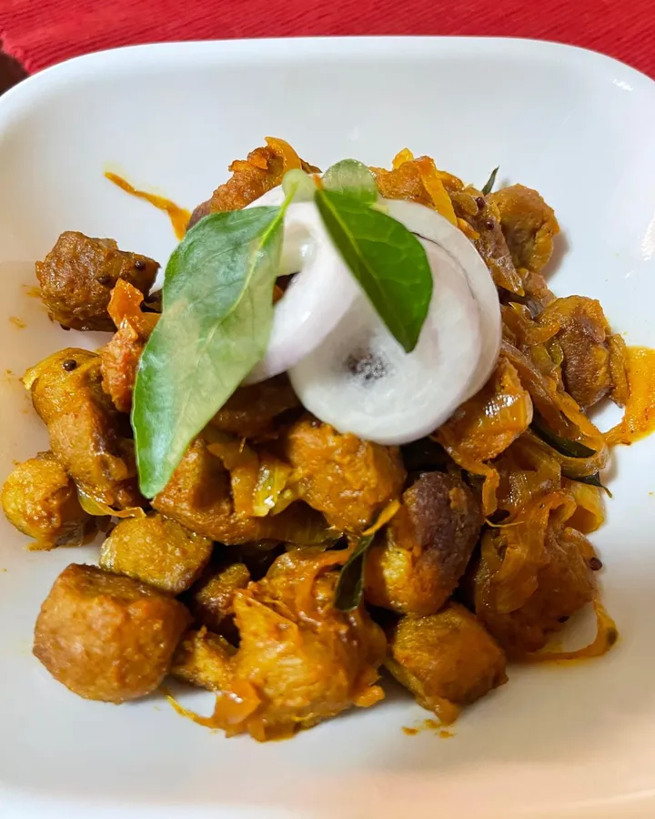 Soy meat chunks with sautéed onions on a white plate, garnished with onion rings and curry leaves