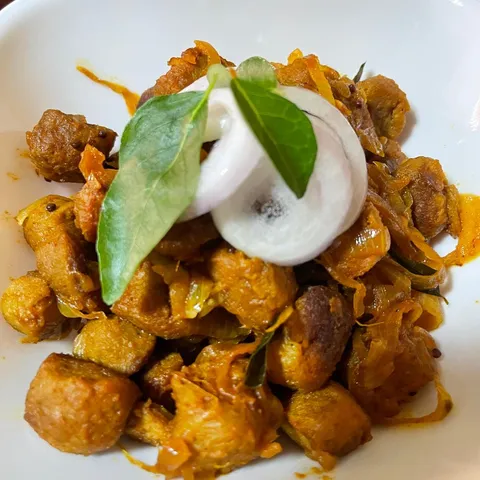 Soy meat chunks with sautéed onions on a white plate, garnished with onion rings and curry leaves