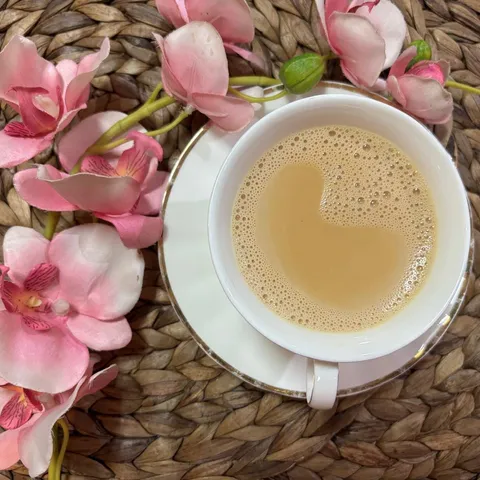 A cup of creamy milk tea on a white saucer, with pink orchids on a woven placemat