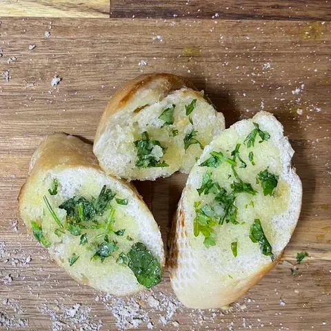 Three slices of garlic bread spread with green herb and garlic butter on a wooden board