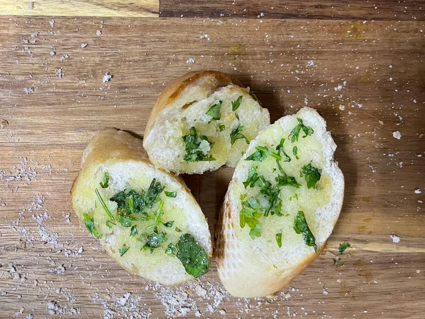 Three slices of garlic bread spread with green herb and garlic butter on a wooden board