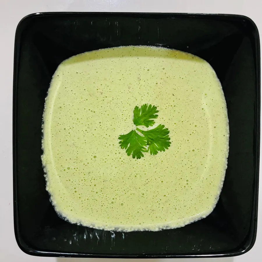 Smooth pale green chutney in a square black bowl, garnished with a single coriander leaf