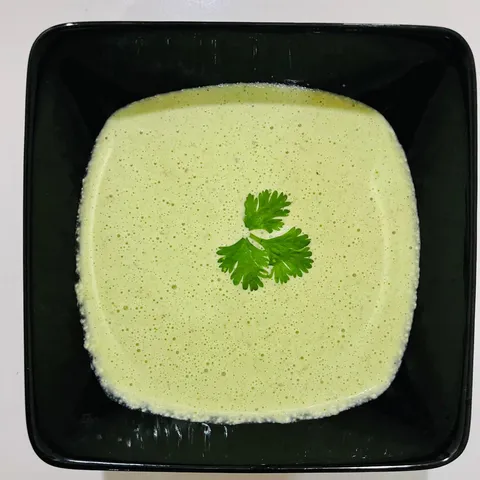 Smooth pale green chutney in a square black bowl, garnished with a single coriander leaf