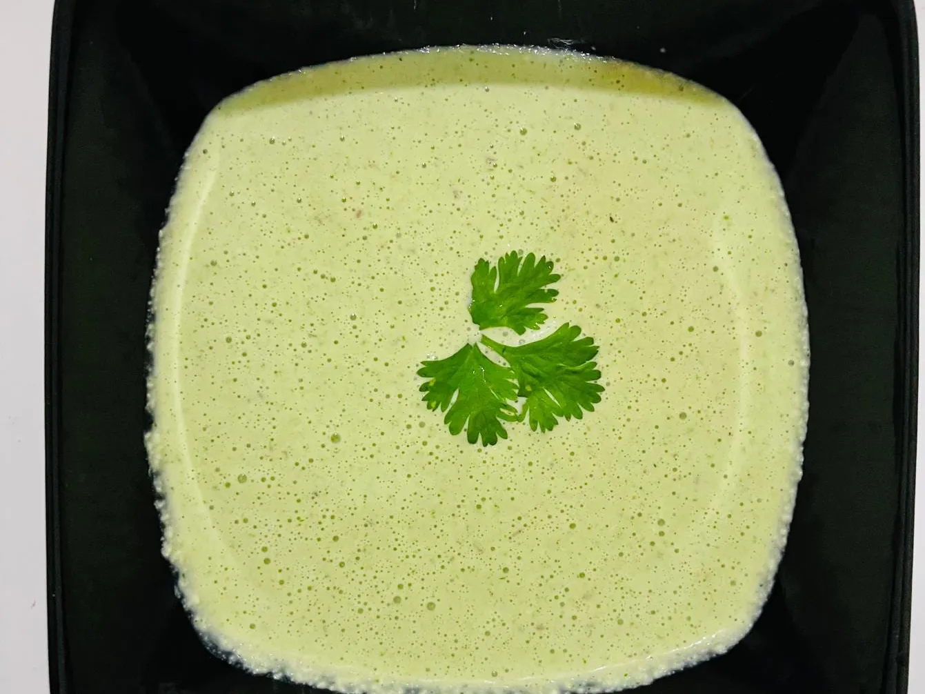 Smooth pale green chutney in a square black bowl, garnished with a single coriander leaf